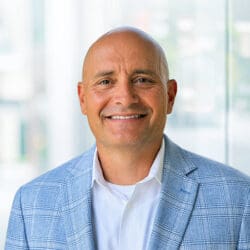 A man (Mike Kirchner) wearing a blue check blazer and white shirt